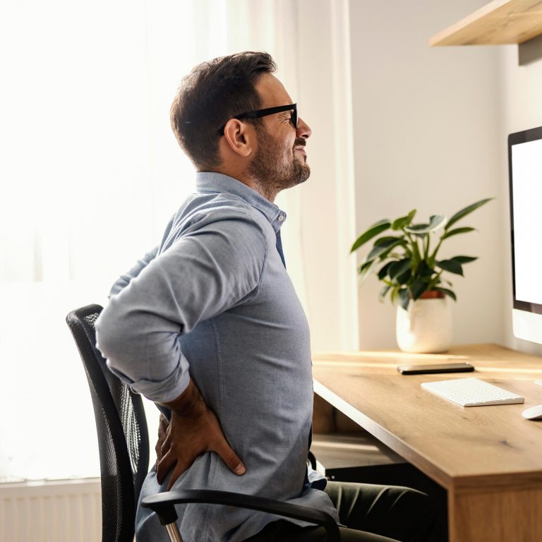 Homem sentindo dor nas costas enquanto trabalha em home office, sinalizando necessidade de avaliação médica.