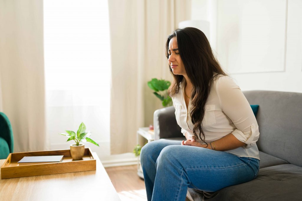 Mulher com forte desconforto pélvico sentado no sofá.