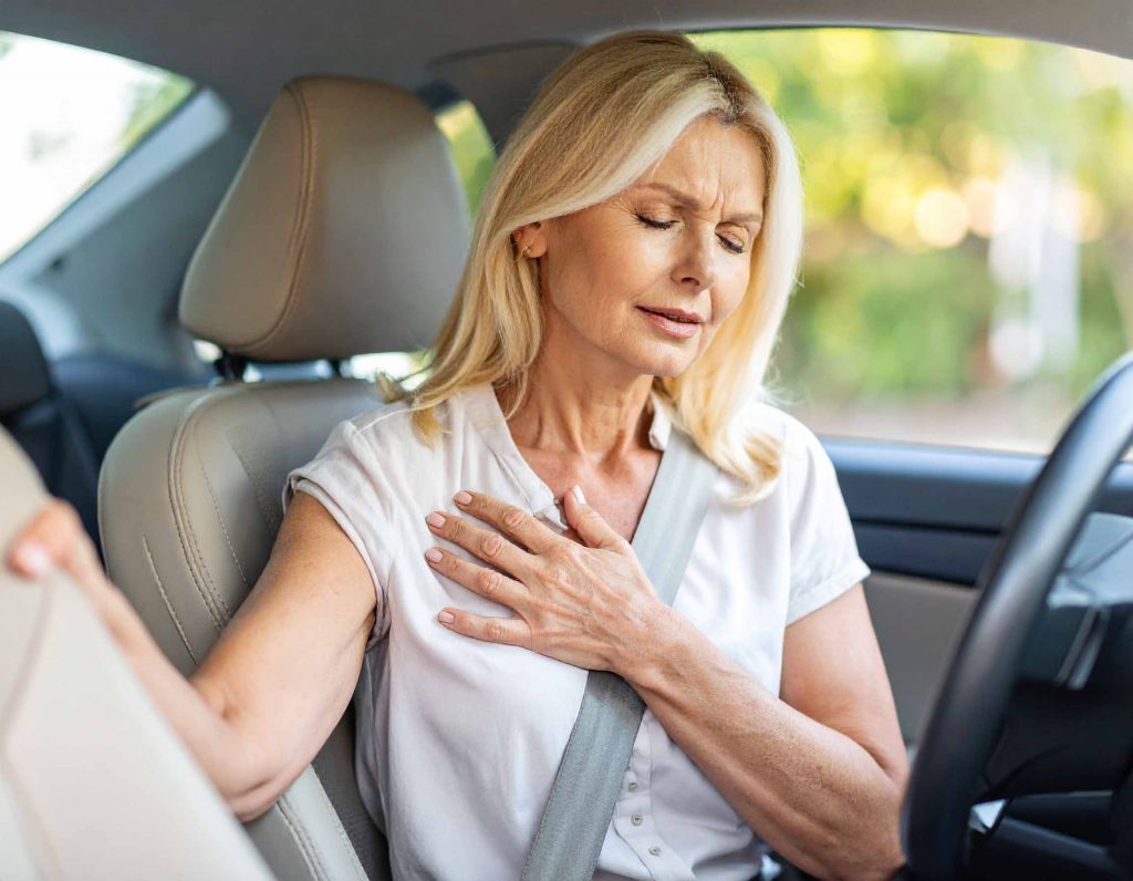 Mulher ao volante com dor no peito, demonstrando possível emergência cardíaca.