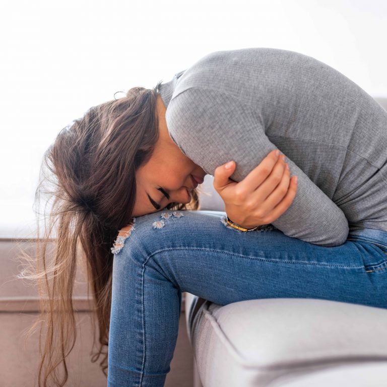 Mulher encolhida no sofá sentindo dor pélvica intensa.