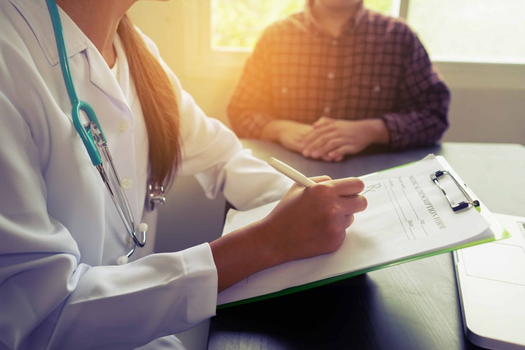 Médica realizando atendimento clínico e preenchendo prescrição durante consulta de rotina