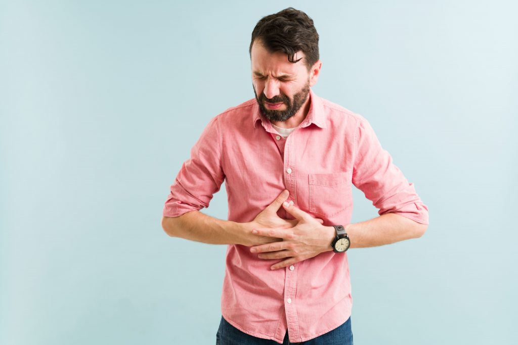 Homem com expressão de dor segurando o estômago, sintoma comum de refluxo gástrico e azia frequente