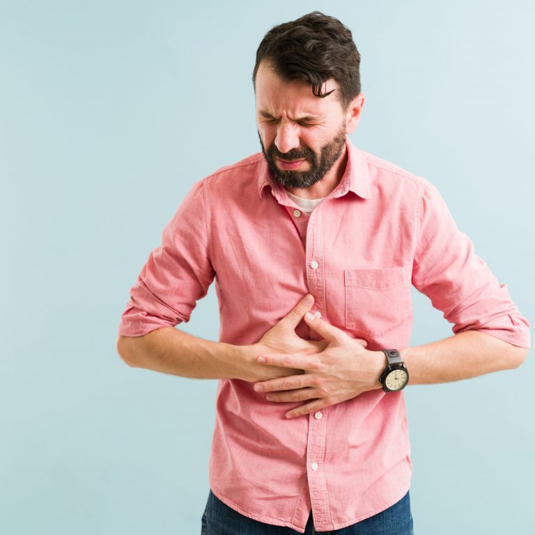 Homem com expressão de dor segurando o estômago, sintoma comum de refluxo gástrico e azia frequente