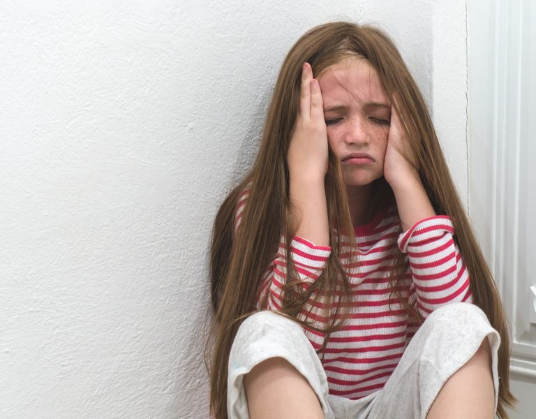 Criança sentada no canto da parede demonstrando tristeza e ansiedade infantil.