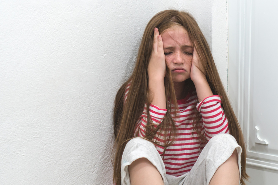 Criança sentada no canto da parede demonstrando tristeza e ansiedade infantil.