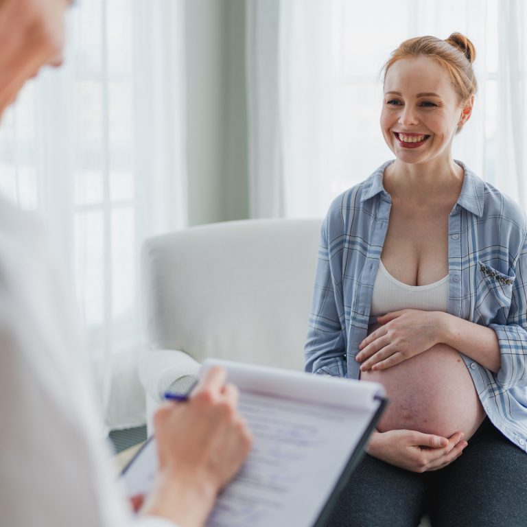 Gestante em casa utilizando celular enquanto se alimenta durante a gravidez.