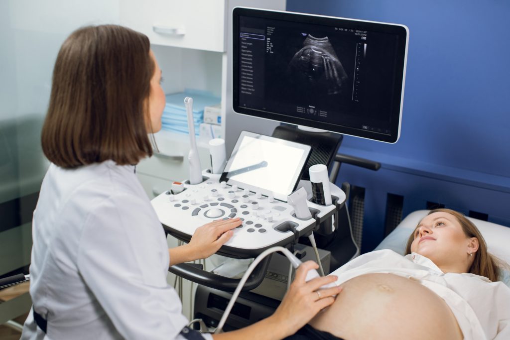 Médica realizando exame de ultrassom em gestante durante consulta de pré-natal.